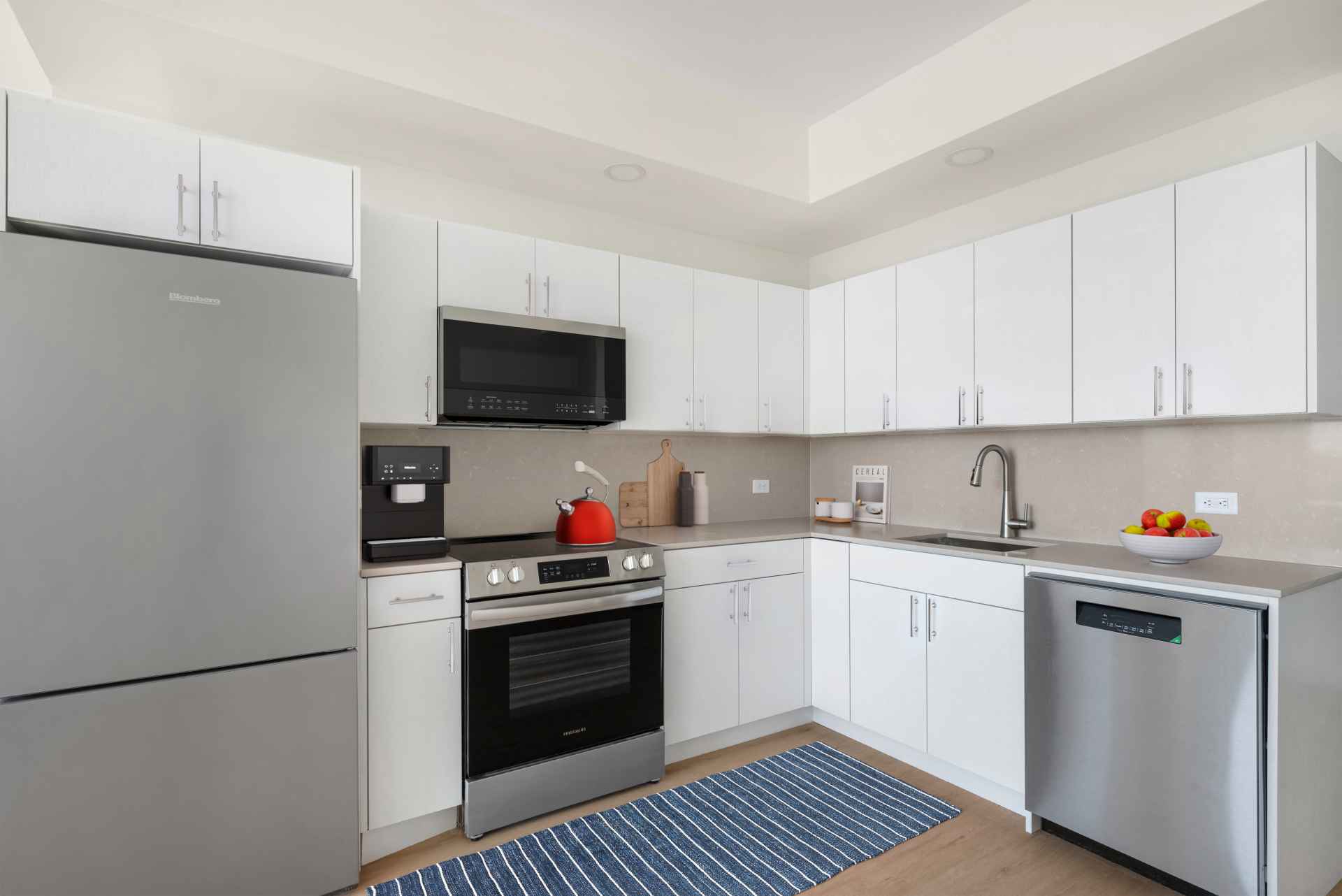 Modern L-shaped kitchen with stainless steel appliances & white cabinets at Tryon North luxury apartments in Inwood.