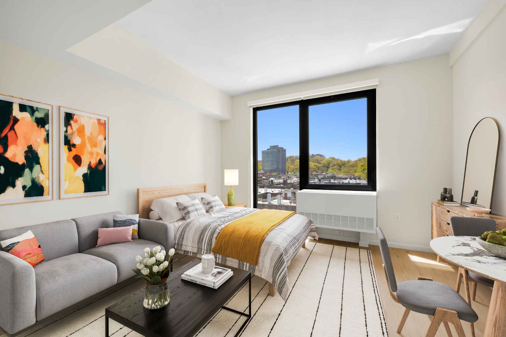 Stylish studio apartment with modern decor featuring bed, couch & dining area at Tryon North new apartments in Inwood NYC.